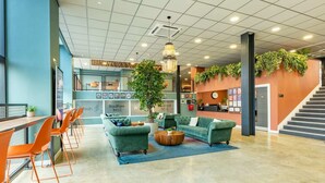 A modern lobby with green sofas, orange chairs, a reception desk, and a staircase. - Student Only Radford Mill (Nottingham)