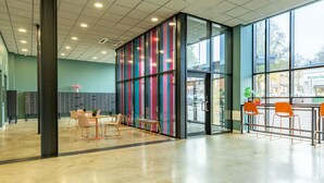 A spacious lobby with a modern design, featuring a seating area with chairs and a table, a large glass door entrance, and a view of the street outside. - Student Only Radford Mill (Nottingham)