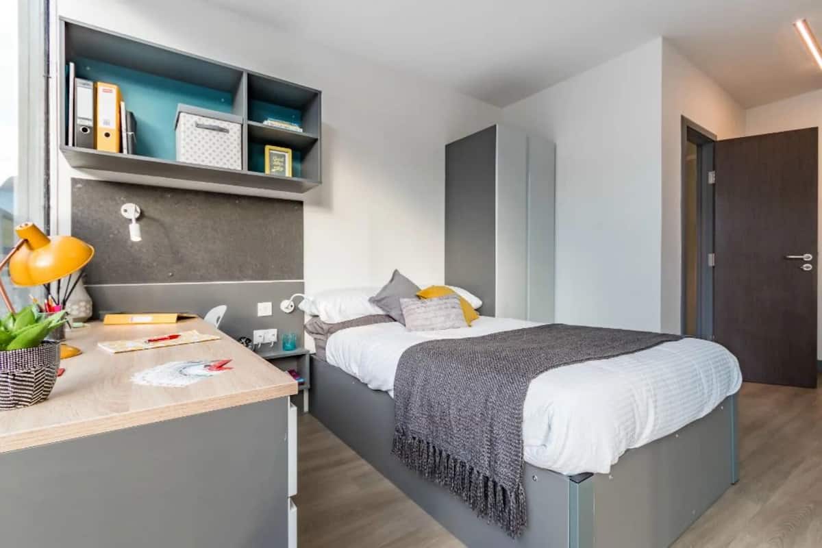 Un dormitorio moderno con cama, mesita de noche, escritorio y estantería.