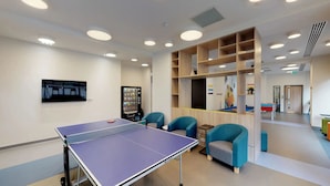 A room with a ping pong table, two blue chairs, a vending machine, and a pool table in the background. - For Students Only Canvas Capital House in Southampton (Southampton)