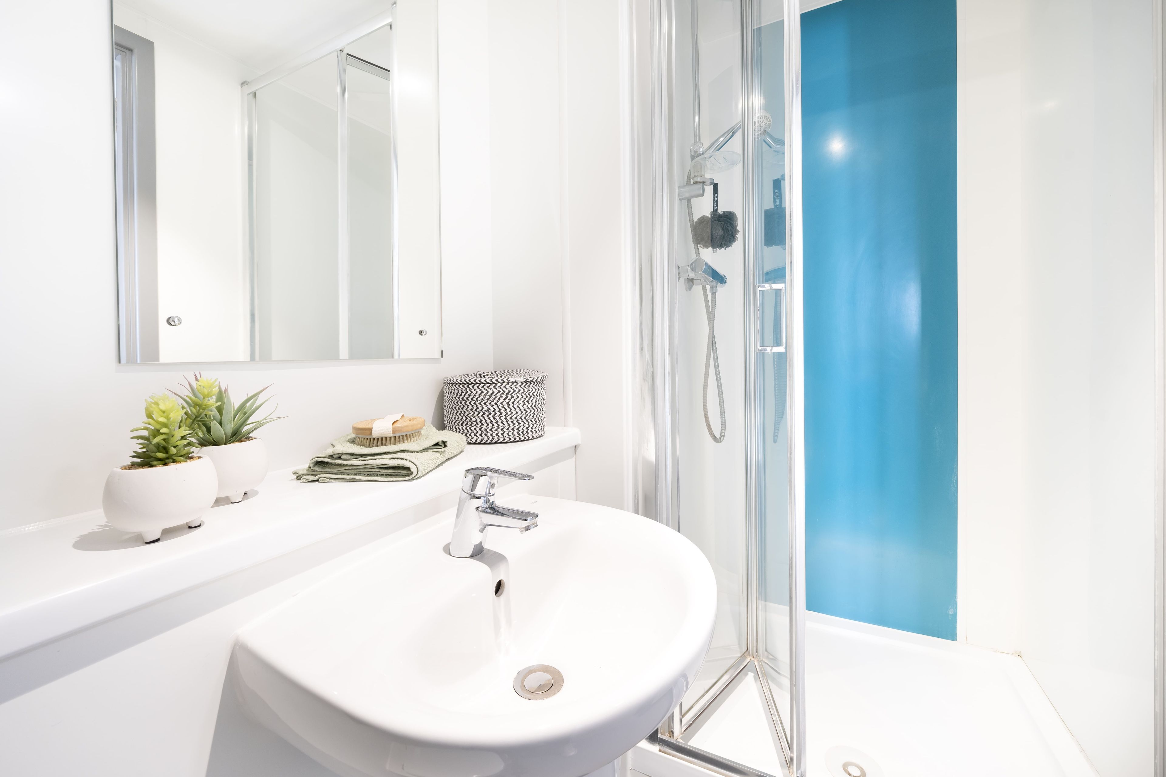 A modern bathroom with a white sink, a shower with a glass door, and a mirror above the sink.