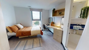 Una camera da letto con un letto, una scrivania, una sedia e un bagno piccolo.