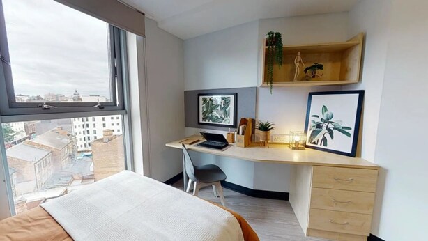 Una camera d'albergo moderna con un letto grande, una scrivania con un portatile, una sedia e vista sulla città dalla finestra.