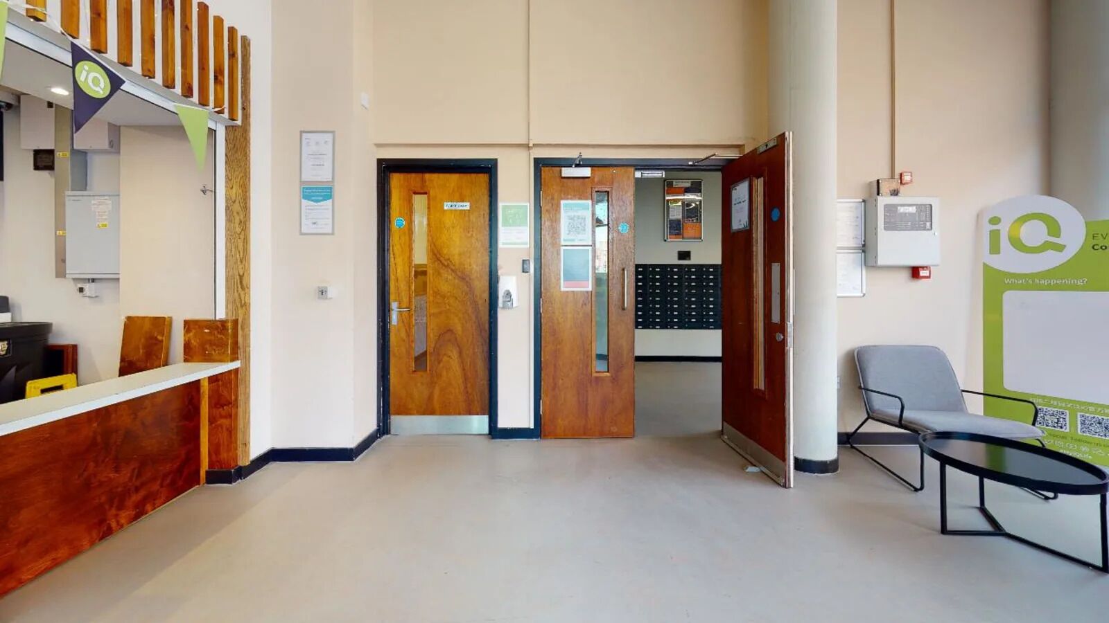 A reception area with a wooden reception desk, two wooden doors, a seating area with a table, and a bulletin board with a QR code.