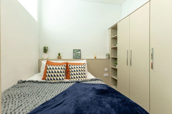Quarto com cama, guarda-roupa e uma pequena estante com plantas.