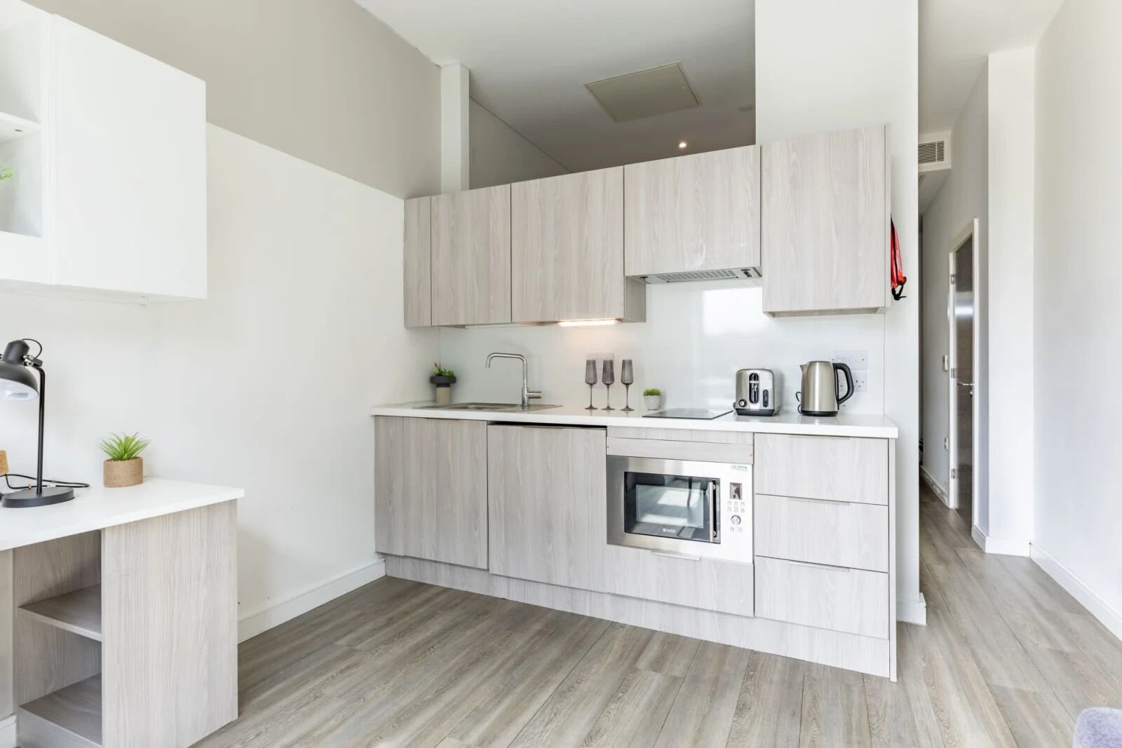 A modern kitchen with light wood cabinets, a built-in oven, and a coffee maker.