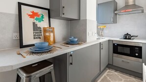 A modern kitchen with grey cabinets, a stainless steel range hood, and a microwave. There is a framed picture on the wall and a jar of pasta on the counter. - Student Only Oldway Centre (Swansea)