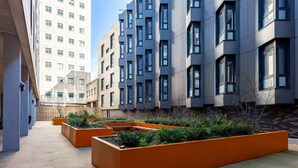 A modern urban courtyard with rectangular planters and a building with multiple windows. - Student Only Oldway Centre (Swansea)