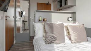 A bedroom with a bed, a mirror, a desk, and a shelf with a clock. - Student Only Oldway Centre (Swansea)