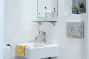 A modern bathroom with a white sink, a glass shelf above the sink, a mirror, and a small potted plant on the wall. - For Students Only - Signal Place - Campus Accommodation (Nottingham)