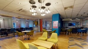A modern cafe with yellow chairs and tables, a blue pillar, and a bar area with bookshelves. - Opal Court (Leicester)