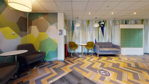 A modern waiting area with geometric patterned walls, a grey sofa, two yellow chairs, and a small table. - Opal Court (Leicester)