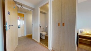 A hallway leading to a bathroom with a toilet, wooden wardrobe, and a small shelf with a picture and candle. - Opal Court (Leicester)