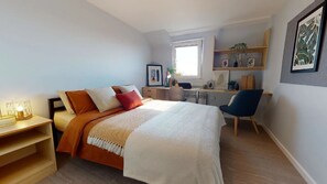 A bedroom with a bed, bedside table, chair, desk, and shelving unit. - Opal Court (Leicester)