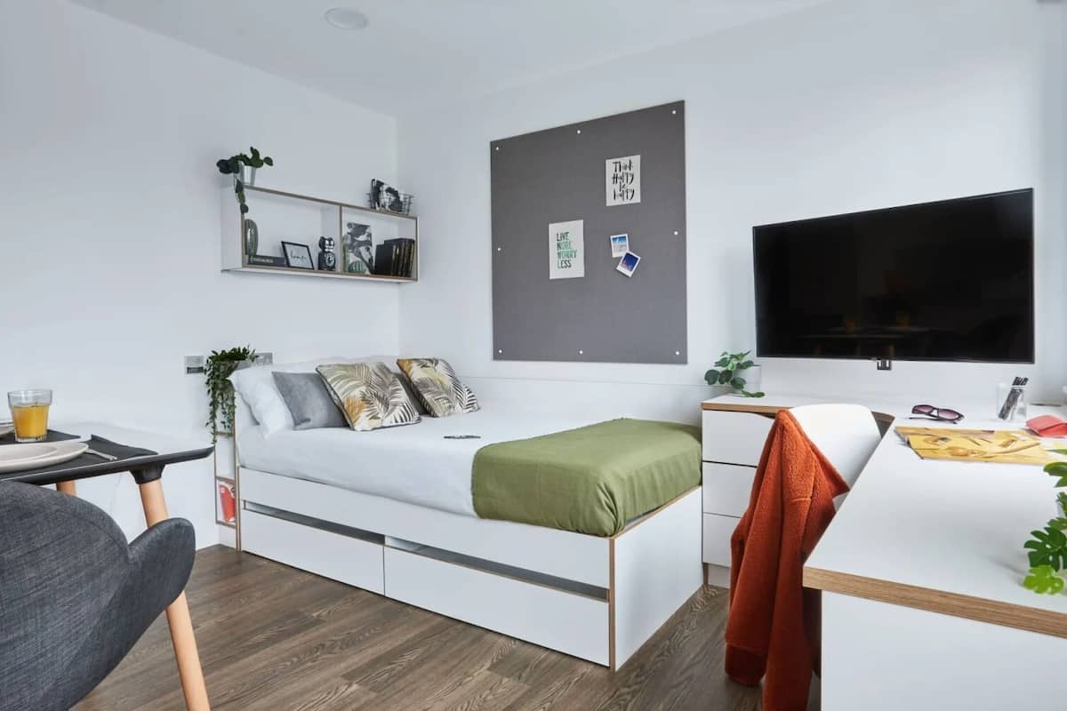 A modern, well-lit room with a bed, a desk, a chair, and a TV.