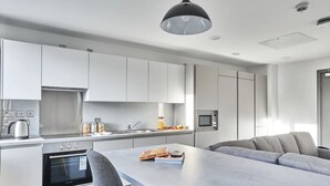Een moderne keuken met witte kasten, een inbouwoven en een eetgedeelte met een grijze tafel en stoelen.