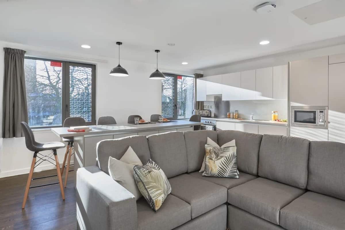 A modern kitchen with white cabinets, a microwave, and a dining area with a gray sofa and chairs.