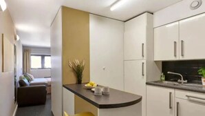 Une cuisine compacte avec un petit îlot central, un coin repas avec une chaise jaune et un coin cuisine.