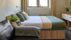 Une chambre d’hôtel de taille réduite, comprenant un lit, un canapé, un bureau et une fenêtre avec des rideaux.