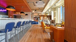 A modern bar area with a long counter, blue bar stools, and yellow seating. - For Student Only Liv Student Sheffield - Campus Accommodation (Sheffield)