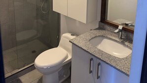 A modern bathroom with a glass shower enclosure, a toilet, a sink with a granite countertop, and a mirror with a wooden frame. - Modern Apartment with Volcano View 901 Santa Tecla (Santa Tecla)