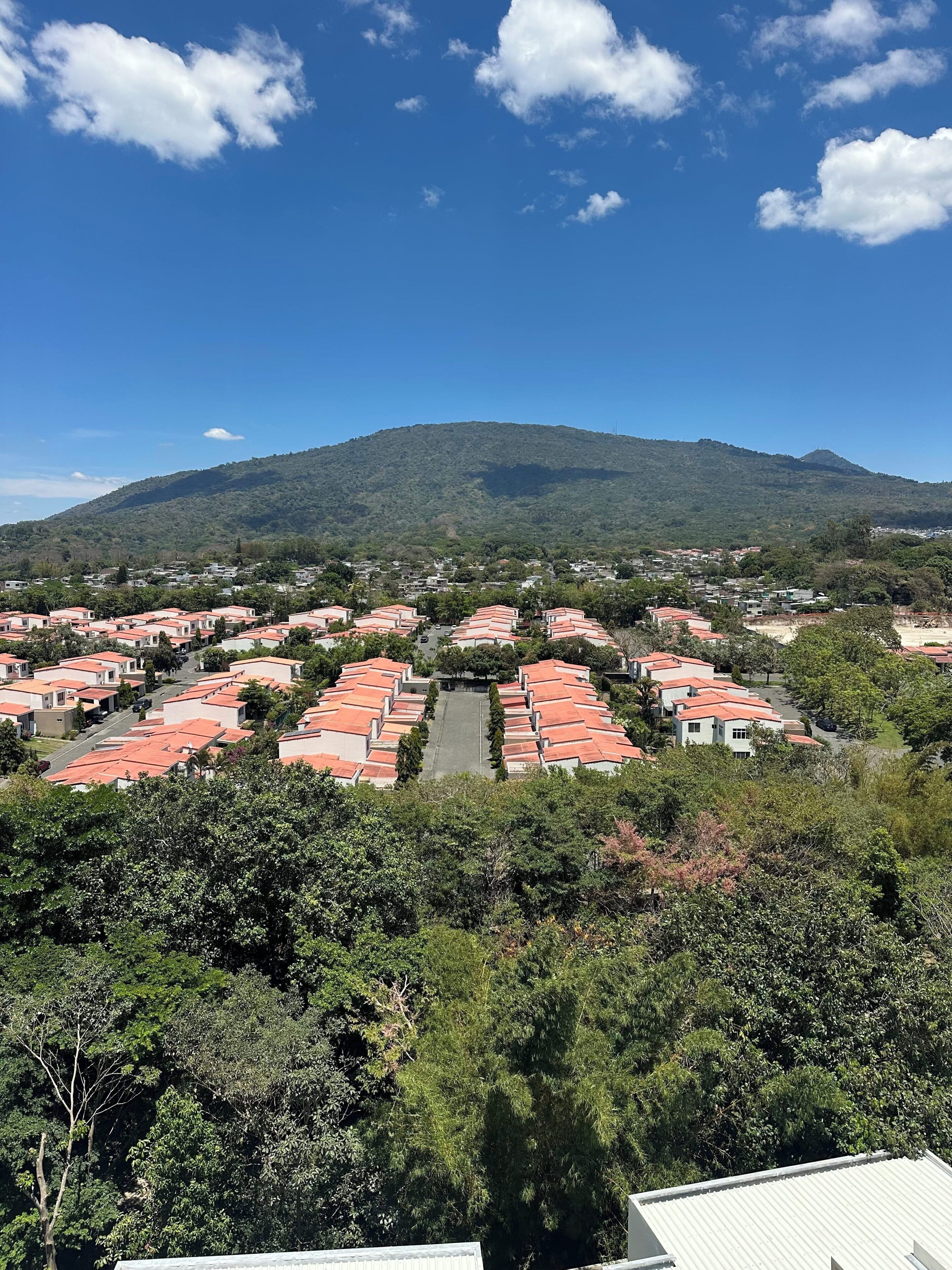 Zona residencial con casas de tejados rojos, una calle central y una montaña al fondo.
