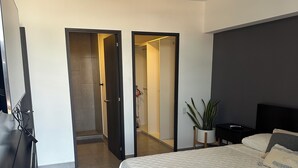 A modern hotel room with a large bed, a dark headboard, a bedside table, a potted plant, and a door leading to a bathroom. - Modern Apartment with Volcano View 901 Santa Tecla (Santa Tecla)