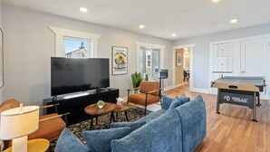 A modern living room with a flat-screen TV, a sofa, a coffee table, and a ping pong table. - The Niche: A cozy perfection!
Newly Renovated Family Friendly! Near Boston (Medford)