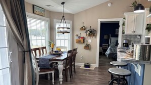 A dining area with a wooden table, chairs, and a blue runner. There is a kitchen area with cabinets and a countertop.