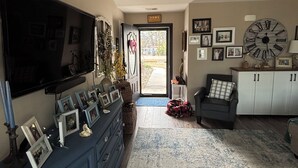 A living room with a television, a large clock, and a door leading outside.
