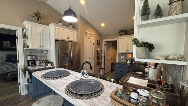 A modern kitchen with a central island, bar stools, a refrigerator, and a pantry.
