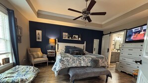 A bedroom with a bed, a chair, a dresser, a television, and a ceiling fan.