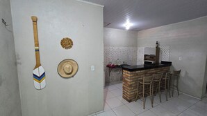 Une cuisine avec un comptoir en briques, deux chaises en osier, un chapeau et une pagaie accrochée au mur.