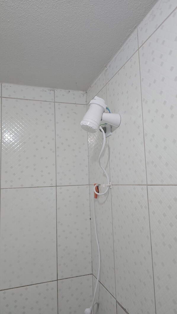 Ducha con cabezal de ducha de mano montado en la pared, conectada a una tubería blanca.
