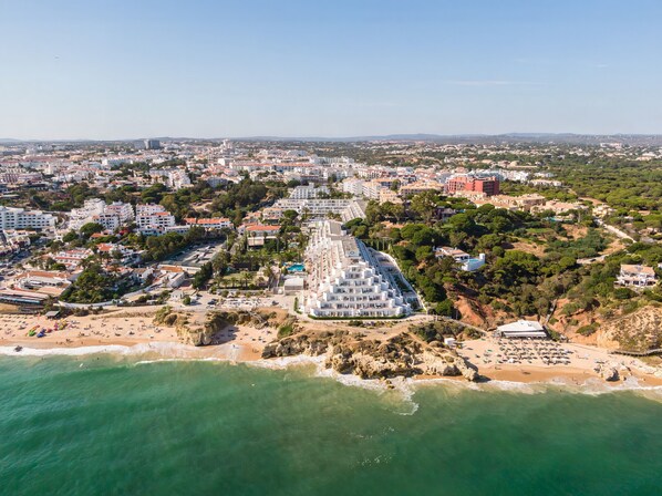 Luftaufnahme einer Küstenstadt mit einem markanten, weißen Gebäudekomplex, einem Strand und umliegenden Wohngebieten.