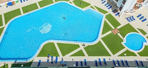 An aerial view of a swimming pool with a unique shape, surrounded by a well-maintained lawn and lounge chairs.
