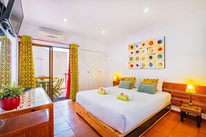 Une chambre d’hôtel comprenant un lit, des tables de chevet, une télévision, un climatiseur, un coin repas avec des chaises et une œuvre d’art colorée accrochée au mur.