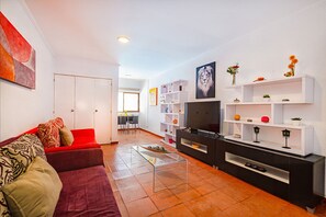 A modern living room with a sofa, coffee table, TV, and shelves with decorative items.