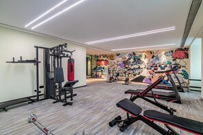 Un gimnasio con equipamiento de levantamiento de pesas, cintas de correr y una pared cubierta de grafitis.