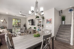 Een moderne woonkamer met een eethoek, een trap en een aan de muur bevestigde televisie.