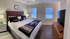 A bedroom with a large bed, two bedside tables with lamps, a dresser, and a television. - Charming 3-Bedroom Retreat with Waterway Access in Hampstead, NC. Hideaway Haven (Hampstead)