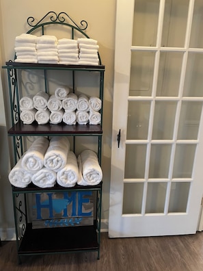 A stylish shelf unit with three tiers holds neatly rolled towels, complemented by a decorative sign.