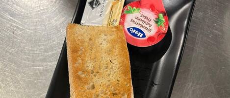 A baguette on a black plate with a knife and a small container of strawberry yogurt.