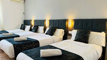 Habitación de hotel con dos camas, cada una con cabecero oscuro y ropa de cama blanca. Hay luces fijadas en la pared sobre las camas y un termostato en la pared.