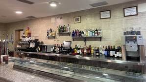 Een bar met meerdere planken vol drankflessen, een biertap en een koelvitrine.