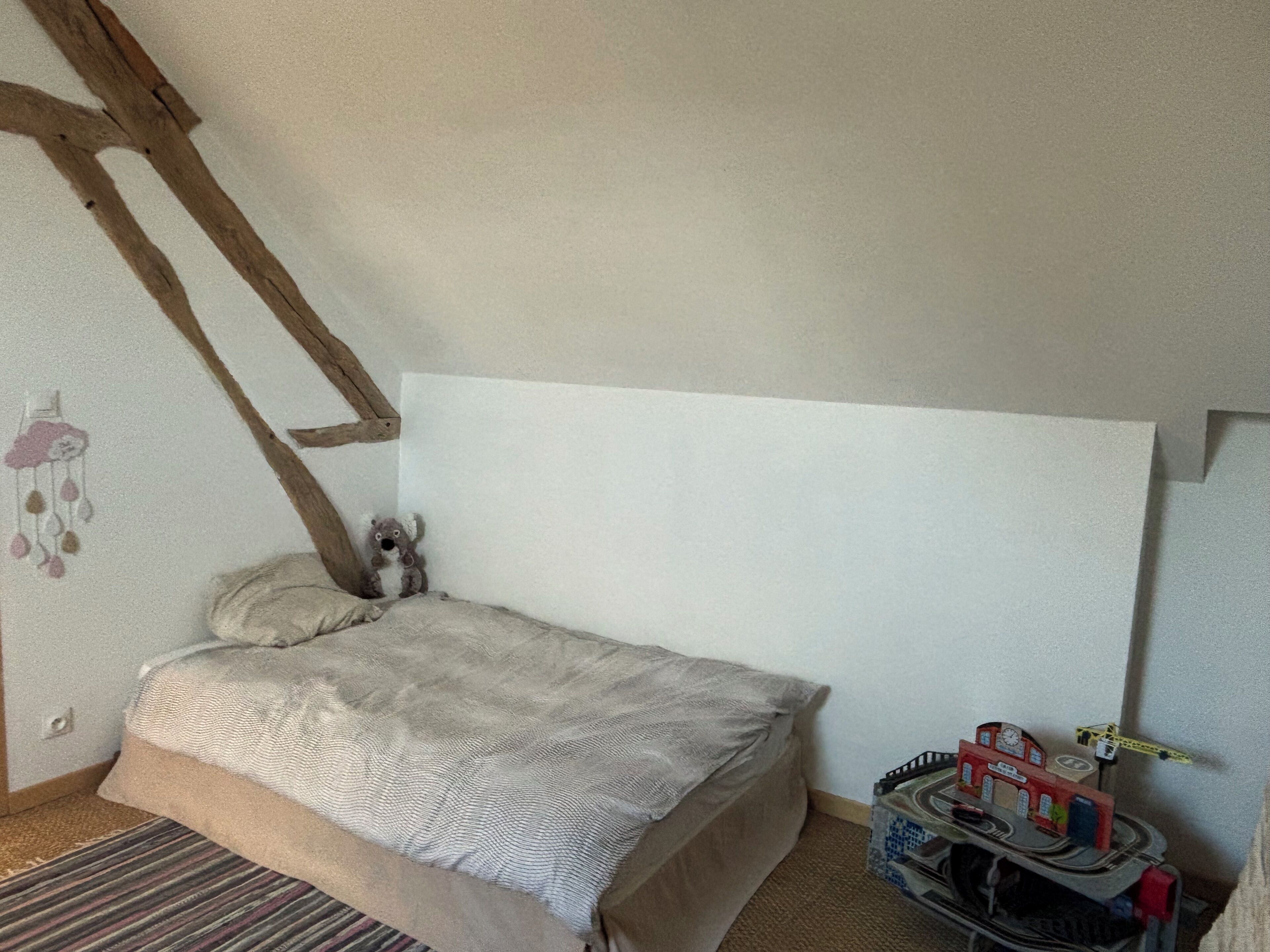 A bedroom with a bed, a small stuffed animal, and a toy train set.