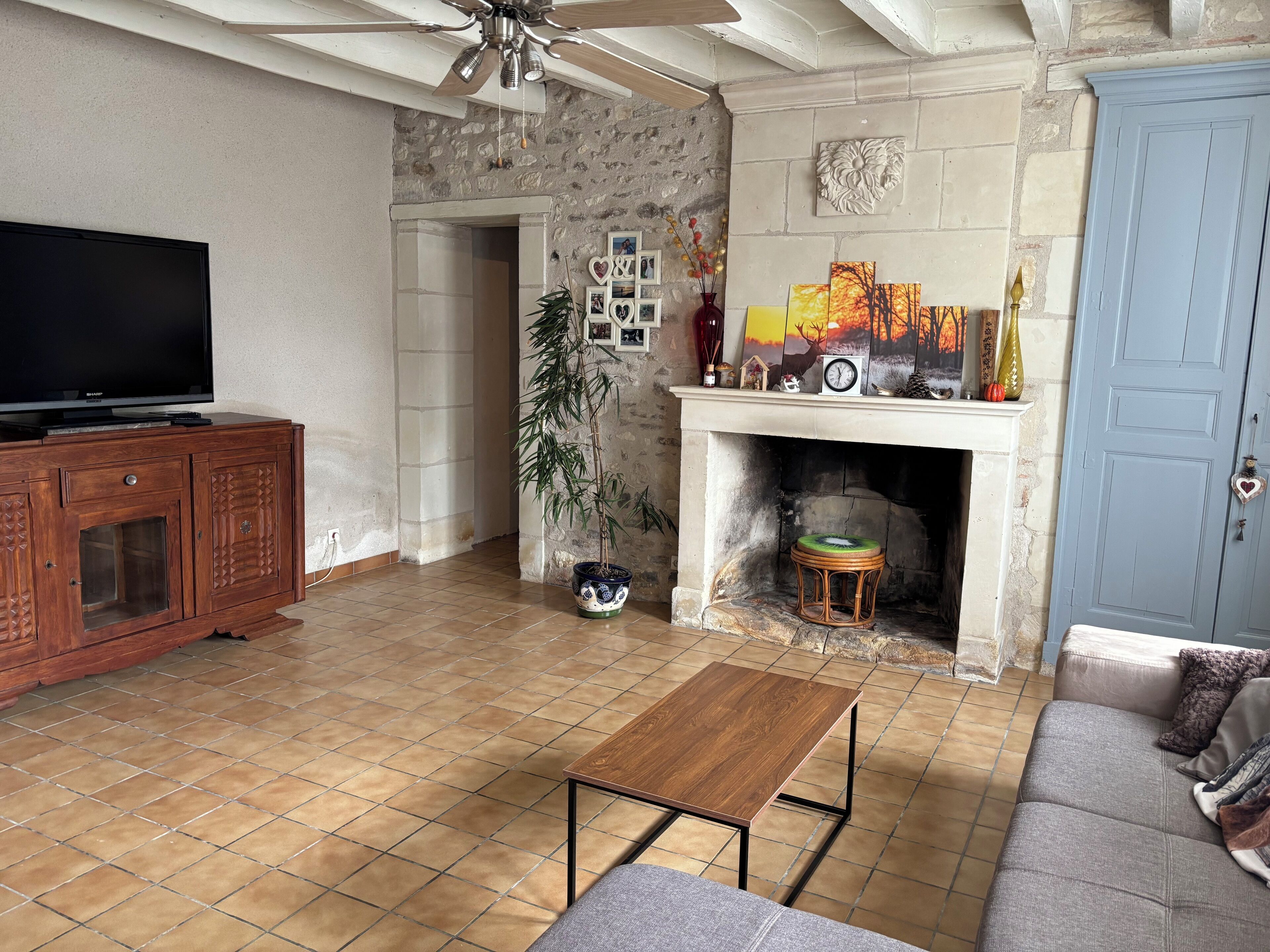 A living room with a television, wooden cabinet, sofa, and a fireplace with decorative items.