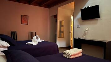 Une chambre d’hôtel avec deux lits, un bureau, une télévision et une porte donnant sur une autre chambre.