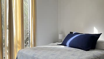Un dormitorio con cama, una silla, una lámpara y una ventana con cortinas.