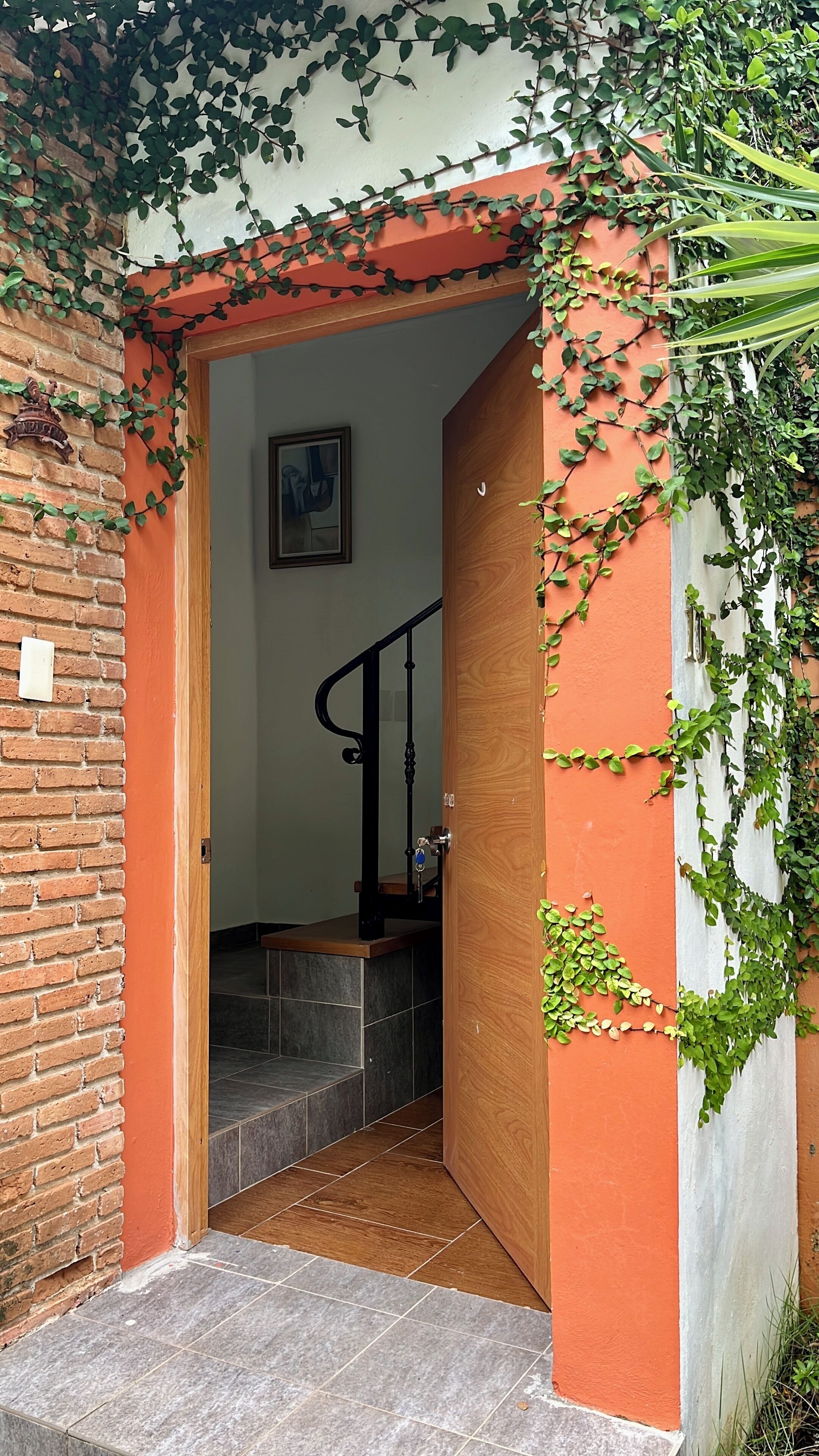 Una escalera conduce a una habitación con pared de ladrillo y puerta de madera.